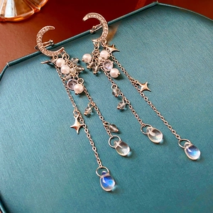 Detailed view of silver moon and star ear clips with dangling pearl fringe on jewelry box