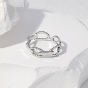Bague chaîne argentée polie présentée sur un socle en plâtre blanc minimaliste
