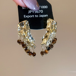 Détail de boucles d'oreilles dorées avec perles œil de tigre sur carte noire