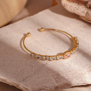 Detail of gold-plated bangle with oval pink and blue zircons on a natural stone surface