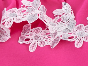 Dettaglio di pizzo floreale bianco con paillettes argentate su tessuto chiffon rosa