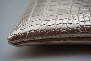 Detailed close-up of champagne gold crocodile-embossed leather and refined edge stitching