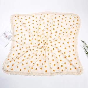 Dettaglio della coperta in mussola di cotone con stampe di arance e bordi con nappe