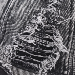 Macro detail of distressed washed denim fabric with ripped holes and frayed white fibers