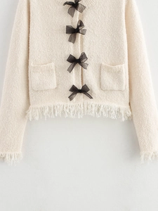 Detail of beige knit cardigan with black bow accents and fringe trim on the cuffs and hem