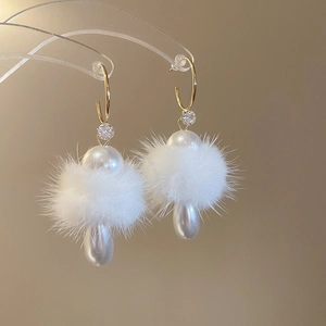 Detail of C-shaped gold earring with white fur pom pom and pearl drop on clear stand