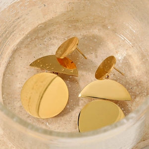 Golden geometric earrings set on textured glass with water droplets in macro view