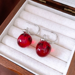 Macro shot of red apple-shaped resin drop earrings with silver hooks in a jewelry box