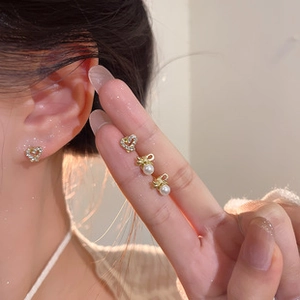 Detailed close-up of golden bow and pearl tassel earrings with heart rhinestones