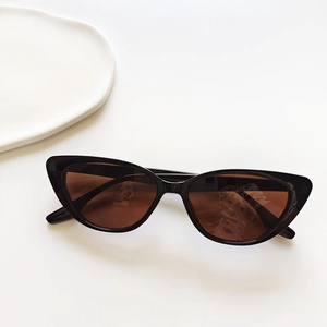 Flat lay of black cat eye sunglasses with dark brown lenses on a minimalist white background
