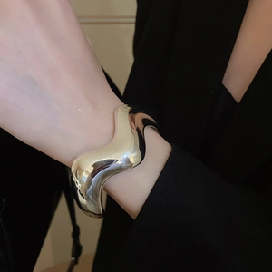 Dettaglio del bracciale rigido ondulato argento lucido su polso con blazer nero elegante