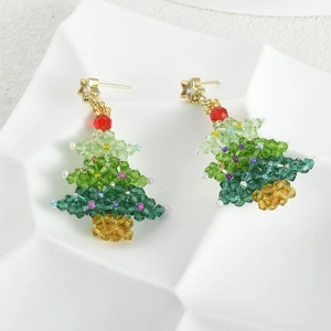 Detailed macro view of handmade Christmas tree crystal beaded earrings on ceramic tray
