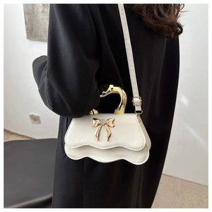 Detailed side view of a white crossbody bag with golden swan handle and bow accent