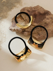 Detailed view of three gold metal elastic hair ties on beach sand with a starfish