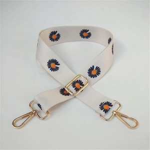 Detail view of adjustable canvas shoulder strap with orange daisy pattern and gold hardware
