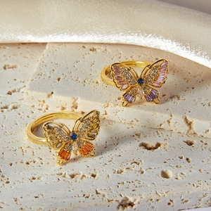 Elegant gold butterfly rings with colorful zircon stones on textured stone and silk