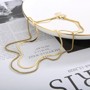 Detailed close-up of a double-layer gold snake and box chain necklace on a white ceramic plate