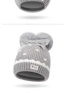 Detail of baby knit hat featuring plush pom-poms, velvet bow, and cute bear badge