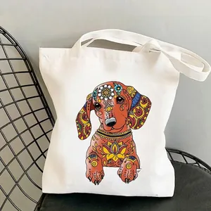 White canvas tote bag featuring colorful mandala dachshund print on a black chair