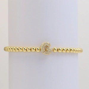 Detailed macro view of gold beaded bracelet featuring a sparkling zircon paved letter G charm