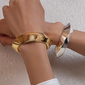Close-up of chunky gold and silver geometric cuffs with mirror-like metallic finish