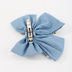 Dettaglio del fiocco in velluto blu con perle e incisione fatta a mano sulla clip a molla