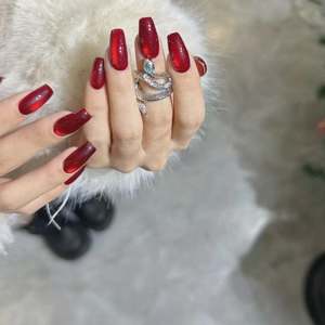 Deep red cat eye press-on nails with silver snake ring on white faux fur background