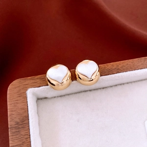 Macro view of gold round stud earrings with white heart inlay on soft velvet surface