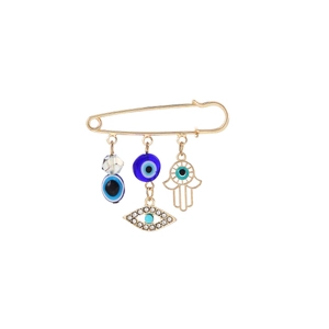 Close-up of golden safety pin brooch with blue evil eye and hamsa hand charms