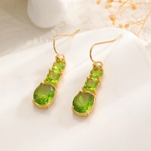 Detail of gold dangle earrings featuring three olive green crystals in various shapes