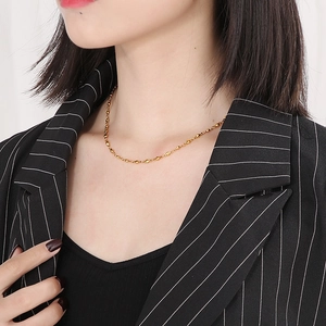Gros plan d'un collier chaîne à perles dorées porté au cou avec un blazer noir