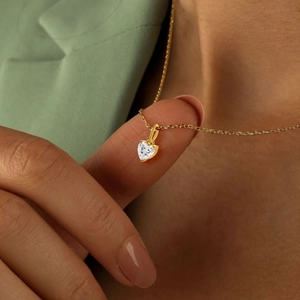 Nahaufnahme eines kleinen Herz-Zirkonia-Anhängers an einer Goldkette in der Hand