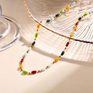 Dettaglio ravvicinato di una collana dorata con perline colorate su vassoio di vetro
