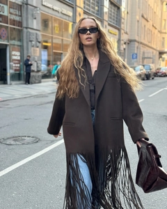 Street style shot of a long dark brown wool coat with fringe trim and notched lapel