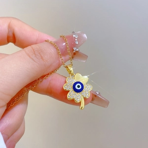 Elegant gold clover necklace with blue eye element and rhinestones held by hand