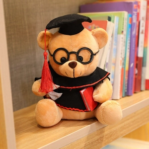 Plush graduation teddy bear with black cap and gown on a wooden bookshelf background