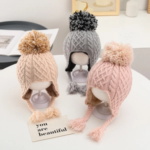 Close-up of knit earflap hats with large pom-poms and warm lining in three colors