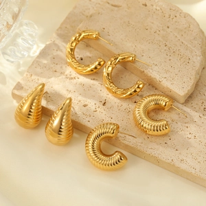 Three pairs of vintage gold textured C-shape and drop earrings on beige stone