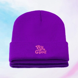 Close-up of pink You are Good embroidery on a purple knitted beanie hat texture