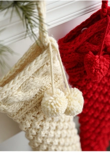 Detail of cable knit Christmas stockings in ivory and red with decorative pompoms