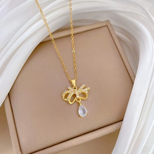 Detail view of a gold bow necklace with clear teardrop pendant on silk lining
