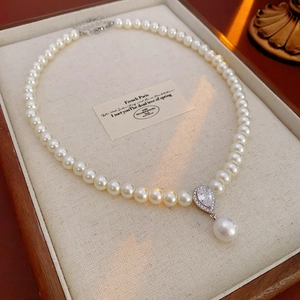 Close-up of a pearl necklace with a teardrop zircon pendant on a beige velvet tray