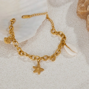 Gold stainless steel chain bracelet with sea shell and starfish charms on a beach sand