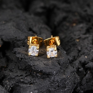 Close-up of gold round cubic zirconia stud earrings set on a dark textured rock surface