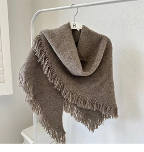 Detail of soft brown knitted shawl with fringe tassels hanging on a white hanger