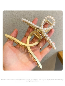 Detail of hand-held gold metal hair claw clip featuring elegant faux pearls and cross design