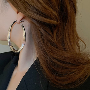 Close-up of large polished silver oval hoop earrings worn by a model for a chic look