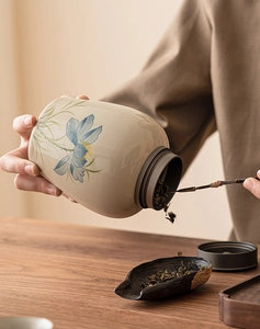 Action shot of tea leaves being scooped from a lotus ceramic canister with a wooden spoon