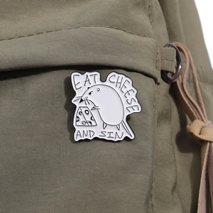 Macro detail of enamel mouse and cheese pin with text on green canvas fabric