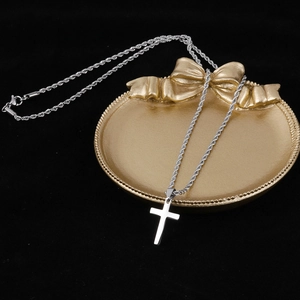 Close-up of a silver cross pendant on a rope chain resting on an ornate gold jewelry tray